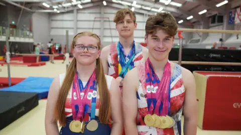 John Fairhall/BBC Grace, Simon and Jack standing in the gym. They are wearing their GB kits and have their necks.