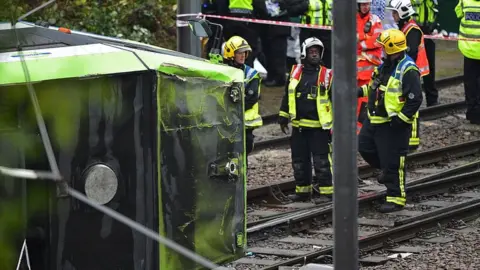 Members of London Fire Brigade look at the overturned tram