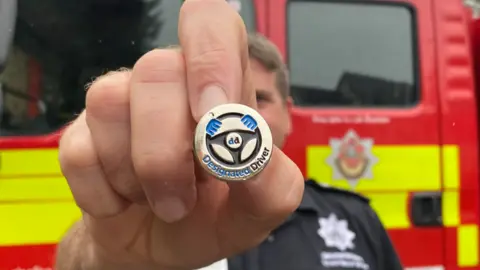 Gloucestershire County Council A firefighter holding the designated driver badge in front of a fire engine