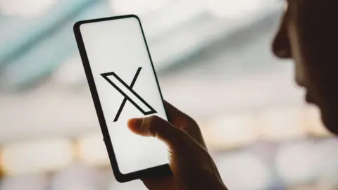 Getty Images A photo illustration of someone looking at the X app on a phone