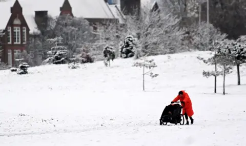 Google A woman pushes her child through a snow covered park in central London