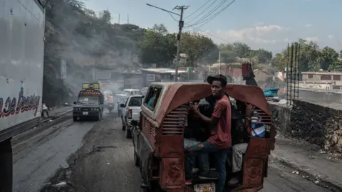 Getty Images A man standing on the open back of a car looks back towards the camera