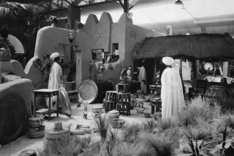 The National Archives Black and white image of artefacts in West Africa pavilion including models of people