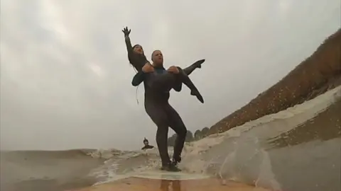 Man holding woman in his arms on a surfboard on the river
