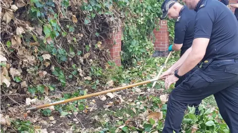 Leicestershire Police Officers scraping back plants to search for evidence