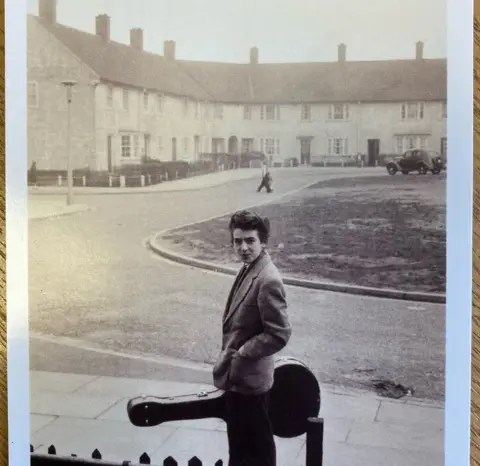 Omega Auctions A young George Harrison holding a guitar case outside his Speke home