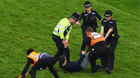 A protester is carried away from track by multiple police