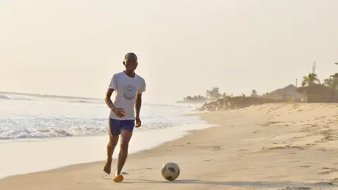 A young man playing football on a beach in Monrovia