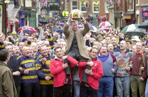 PA Media Prince Charles being lifted up holding the ceremonial ball before starting the ancient Royal Shrovetide Football game, in Ashbourne, Derbyshire