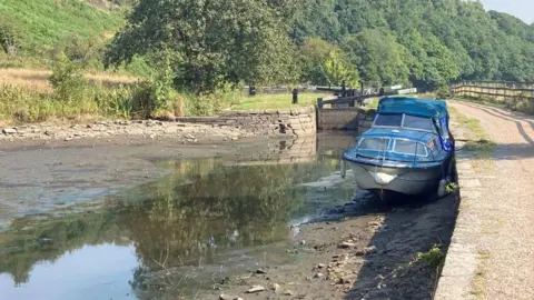 PA Media A boat sits in the dried up Huddersfield narrow canal in West Yorkshire