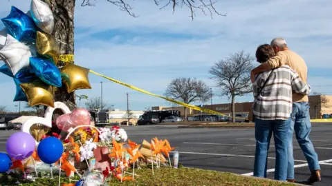 Getty Images A couple hug by a memorial of flowers, balloons and candle set up by a tree across the Walmart where the shooting took place in Chesapeake, Virginia.