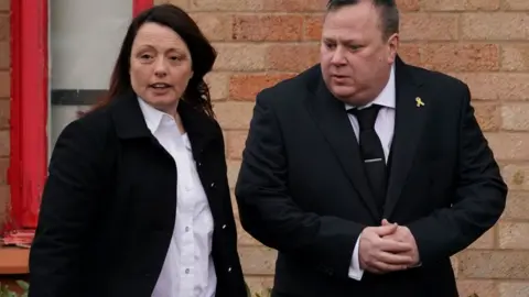 PA Media Leah Croucher's parents Claire and John Croucher watch as her funeral cortege prepares to leave