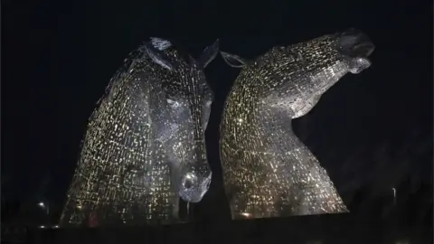 PA Media The Kelpies in Falkirk, Central Scotland, as they are lit up yellow