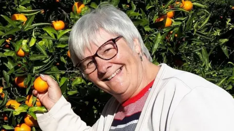 Winn family Jane Winn pictured picking oranges from a tree and smiling at the camera