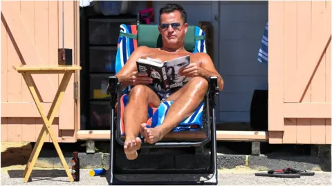 Getty Images A man reading a book in the sunshine while on holiday