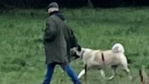 Gloucestershire Police Man in dark green coat with flat cap walking a dog with yellow fur
