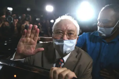 Getty Images Malaysia's former prime minister Najib Razak waves as he leaves the Duta Court complex after he was found guilty in his corruption trial in Kuala Lumpur on July 28, 2020.