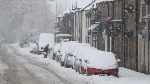 PA Media A motorist brushes snow off a car in Braco near Dunblane