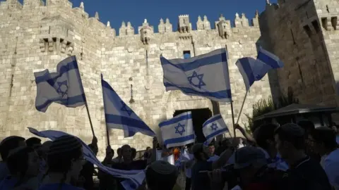 EPA Israeli nationalists wave Israeli flags outside the Damascus Gate of Jerusalem's Old City (15 June 2021)