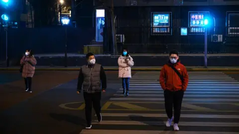 Getty Images Four people cross the road wearing medical masks in Beijing, China