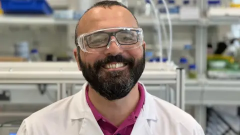 Prof Enrico Andreoli in a lab wearing a lab coat and safety glasses.