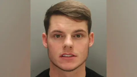 Merseyside Police Ryan Ferguson. He has brunette hair which is pushed to one side. He is looking directly at the camera and showing his teeth, with his mouth open slightly.