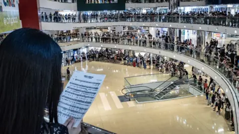 Getty Images Residents and protesters sing songs and shout slogans as they gather at a shopping mall after business hours in Tai Koo district