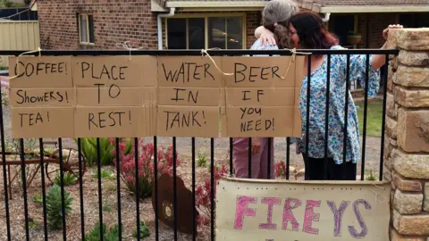 Getty Images Neighbours in Nana Glen embrace outside their homes after returning after the bushfire