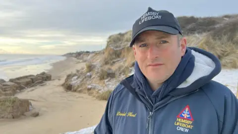 Martin Barber/BBC Daniel Hurd pictured next to eroding cliffs in Hemsby