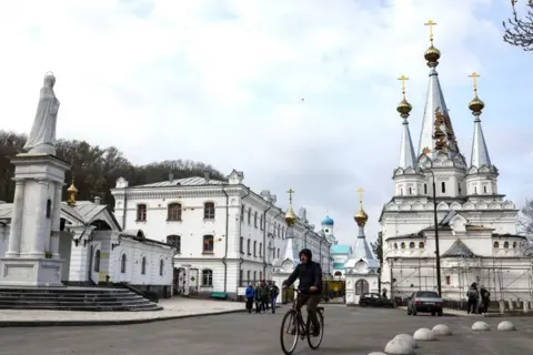 RONALDO SCHEMIDT A man ride his bicycle near the damaged Sviatohirsk Cave Monastery, an Orthodox Christian monastery on the bank of the Seversky Donets River near the town of Sviatohirsk (Svyatohirsk)