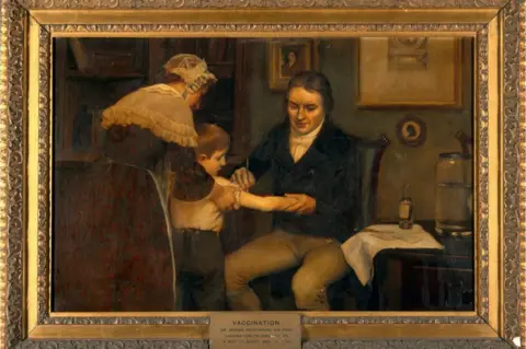 Wellcome Collection Oil painting in a gold frame depicting Edward Jenner administering his first vaccination to a young boy James Phipps