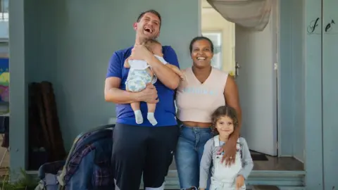 Daniela, Rafael and their two young children stand in front of their tiny house