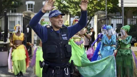 Getty Images A police officer dances with a group of performers during the Notting Hill Carnival