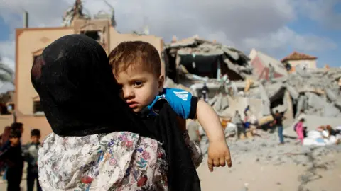 A Palestinian child is carried by a woman at the site of an Israeli strike on a house in Rafah, in the southern Gaza Strip (5 May 2024)