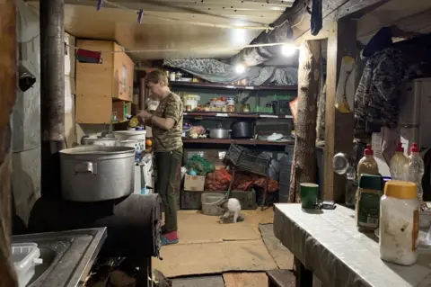 A Ukrainian soldier prepares food in a makeshift kitchen near the front lines