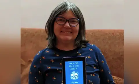 Contributor image Clare Fayer holding a kindle displaying Mckenzy's novel Why the Good Die Young