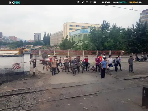 NK NEWS Masked citizens wait for a train to pass at a crossing in Phyongysong, North Korea