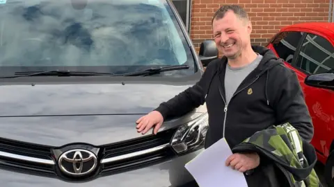 Nick Daniels Nick Daniels standing in front of the new car he bought while waiting for his scrappage grant payment.