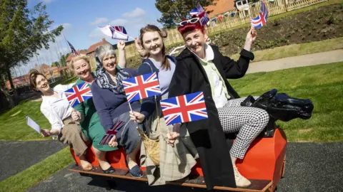 Beamish Museum Five women in 1950s clothing sit on a sliding horse playground equipment