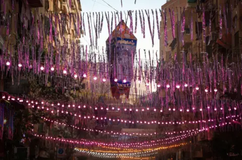 Getty Images Lights and tinsel hang across a street.
