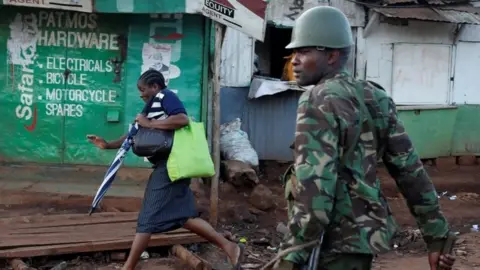 Reuters A woman runs in front of a policeman during clashes between opposition supporters and police in Kawangware slum in Nairobi (30 October 2017)