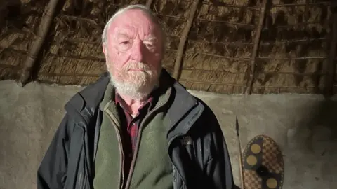 Emma Baugh/BBC Francis Pryor in a roundhouse at Flag Fen
