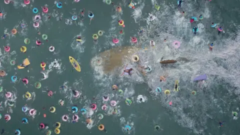 Courtesy of Warner Bros. A large shark swims beneath holidaymakers on inflatables in the ocean