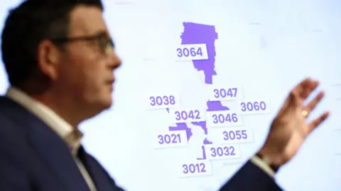 Getty Images Victorian premier Daniel Andrews stands in front of a powerpoint slide listing the postcode hotspots on a map