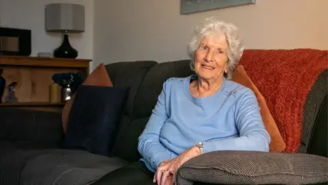 NHS Somerset Sylvia Selway sitting on a sofa at home