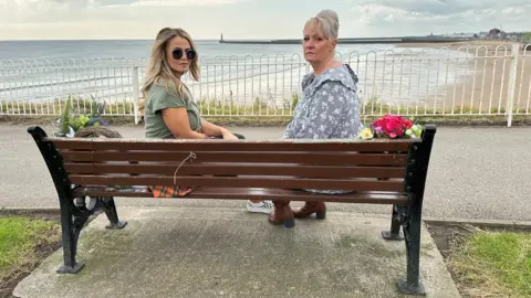 BBC Two women sit on a bench overlooking the sea