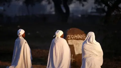 Three women in white kneeling down praying in Harare