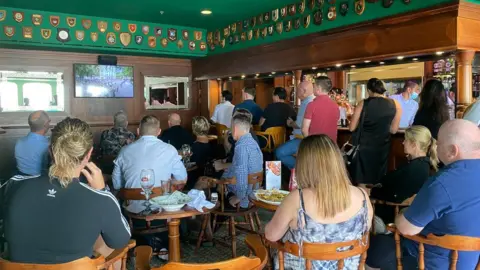 People watch the funeral service in a bar on the hotel and former ocean liner, QE2