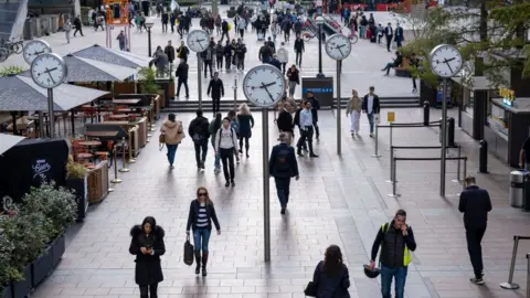 Mike Kemp Commuters walking past world clocks in a square in Canary Wharf.