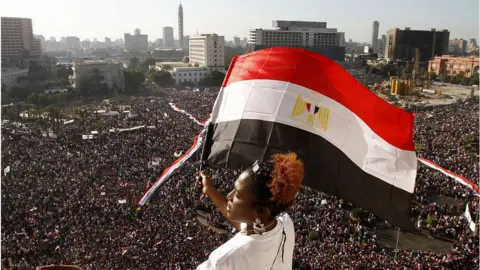 Getty Images A woman waves an Egyptian flag overlooking crowds in Tahrir Square, Cairo (Feb 2011)